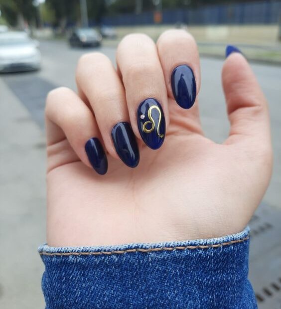 Esmalte de uñas azul oscuro con arte minimalista del signo Leo en uñas redondas medianas