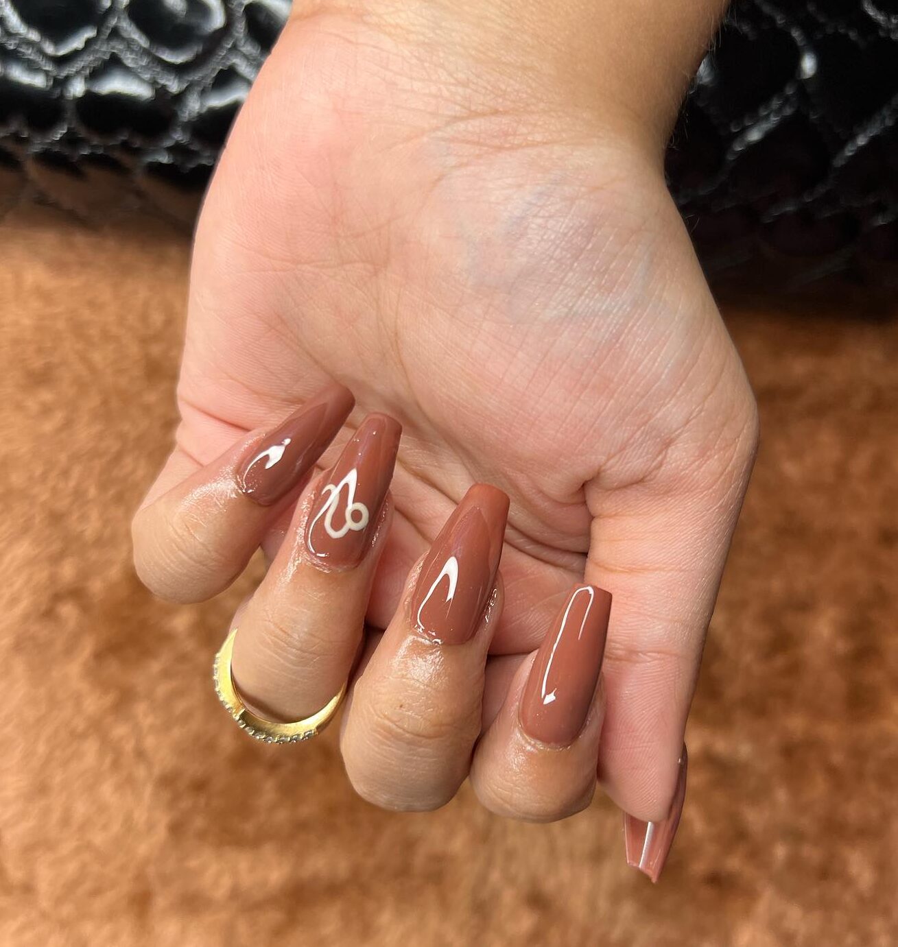 Esmalte de uñas marrón brillante con arte de uñas minimalista con el signo de Leo en uñas largas de ataúd