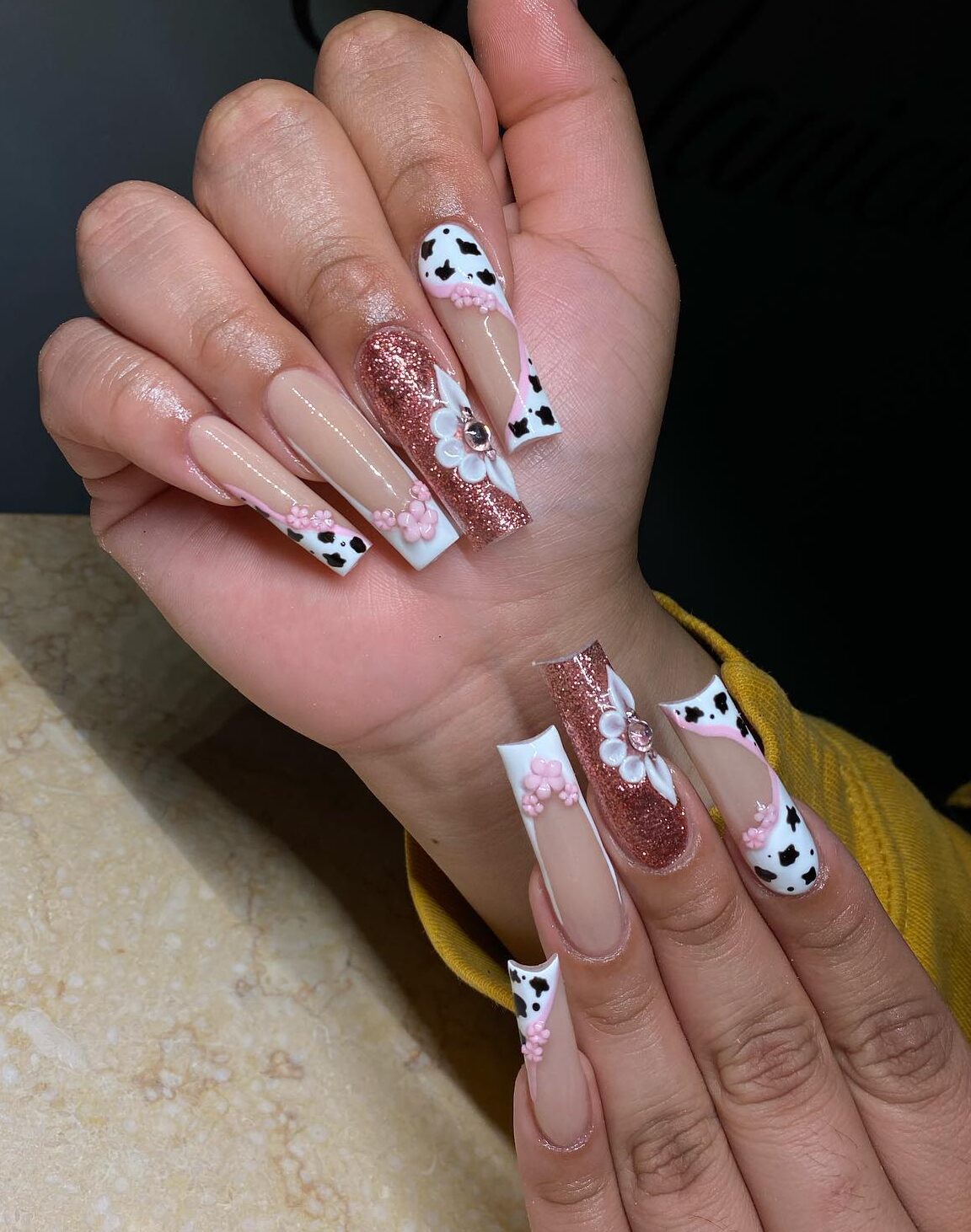 Esmalte de uñas blanco y oro rosa con estampado de vaca y flores en 3D en uñas largas y cuadradas.