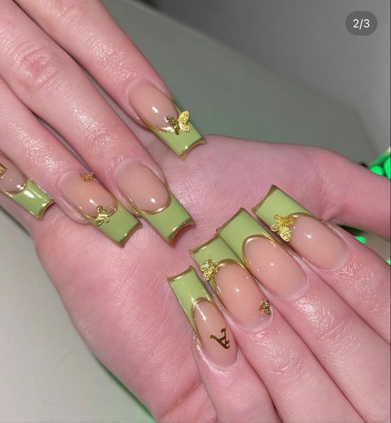 Puntas francesas de color verde claro con contornos dorados y mariposas doradas en 3D en uñas acrílicas largas y cuadradas.