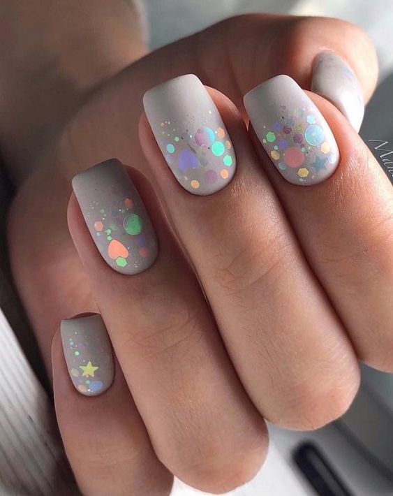 Esmalte de uñas gris claro en acabado mate con brillos en uñas cortas cuadradas