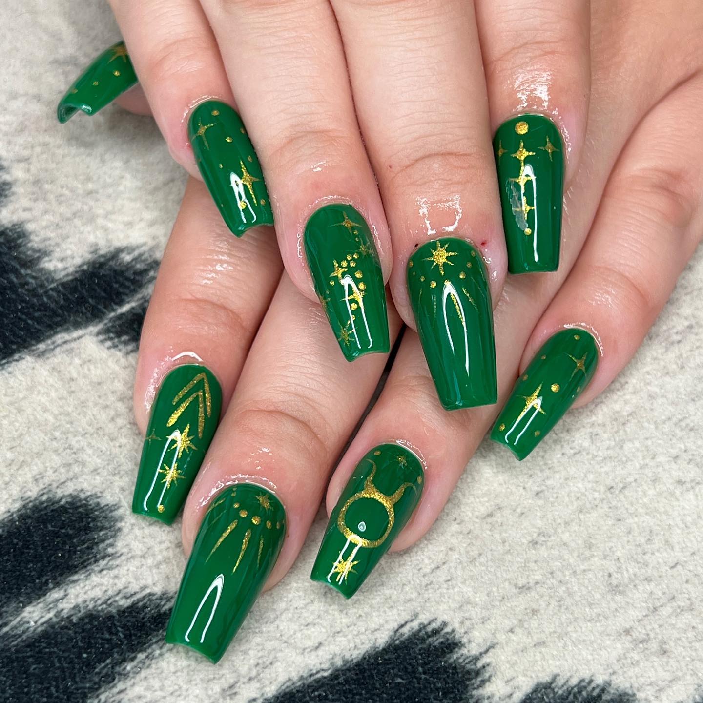 Esmalte de uñas de color verde oscuro con acabado brillante con el signo de Tauro y elementos celestiales en uñas largas de ataúd