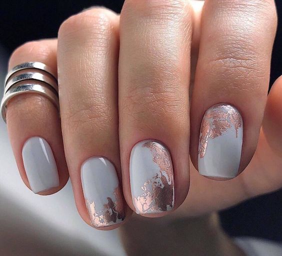 Esmalte de uñas gris claro con decoración de uñas con lámina de oro rosa en uñas cortas y cuadradas