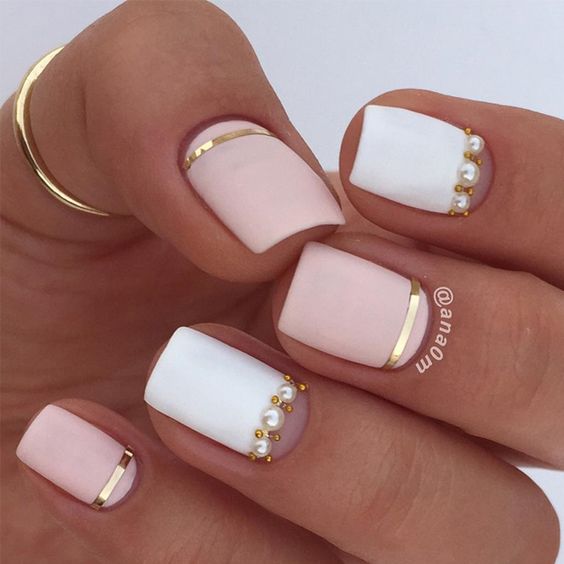 Esmalte de uñas blanco y rosa claro en acabado mate con líneas doradas y perlas en uñas cortas cuadradas