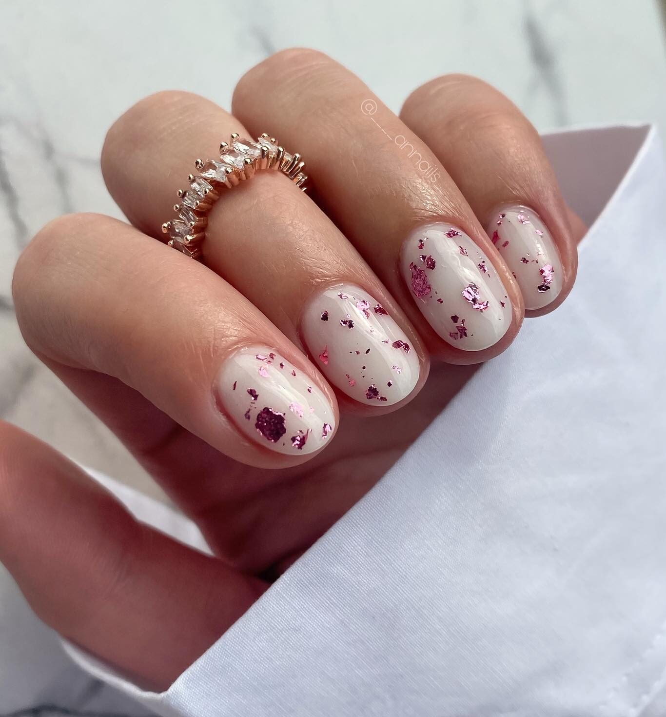 Esmalte de uñas blanco con lámina de oro rosa en uñas cortas y redondas.