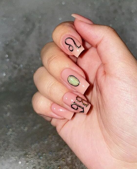 Color de uñas neutro con decoración de uñas con el signo Leo dorado en uñas cuadradas cónicas medianas