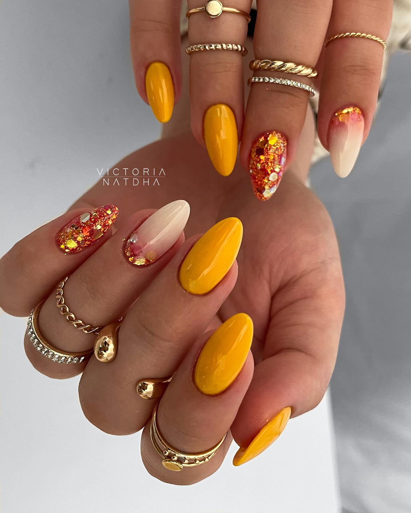 Colores de uñas de color amarillo brillante y blanco pálido con brillos brillantes en uñas largas y redondas.