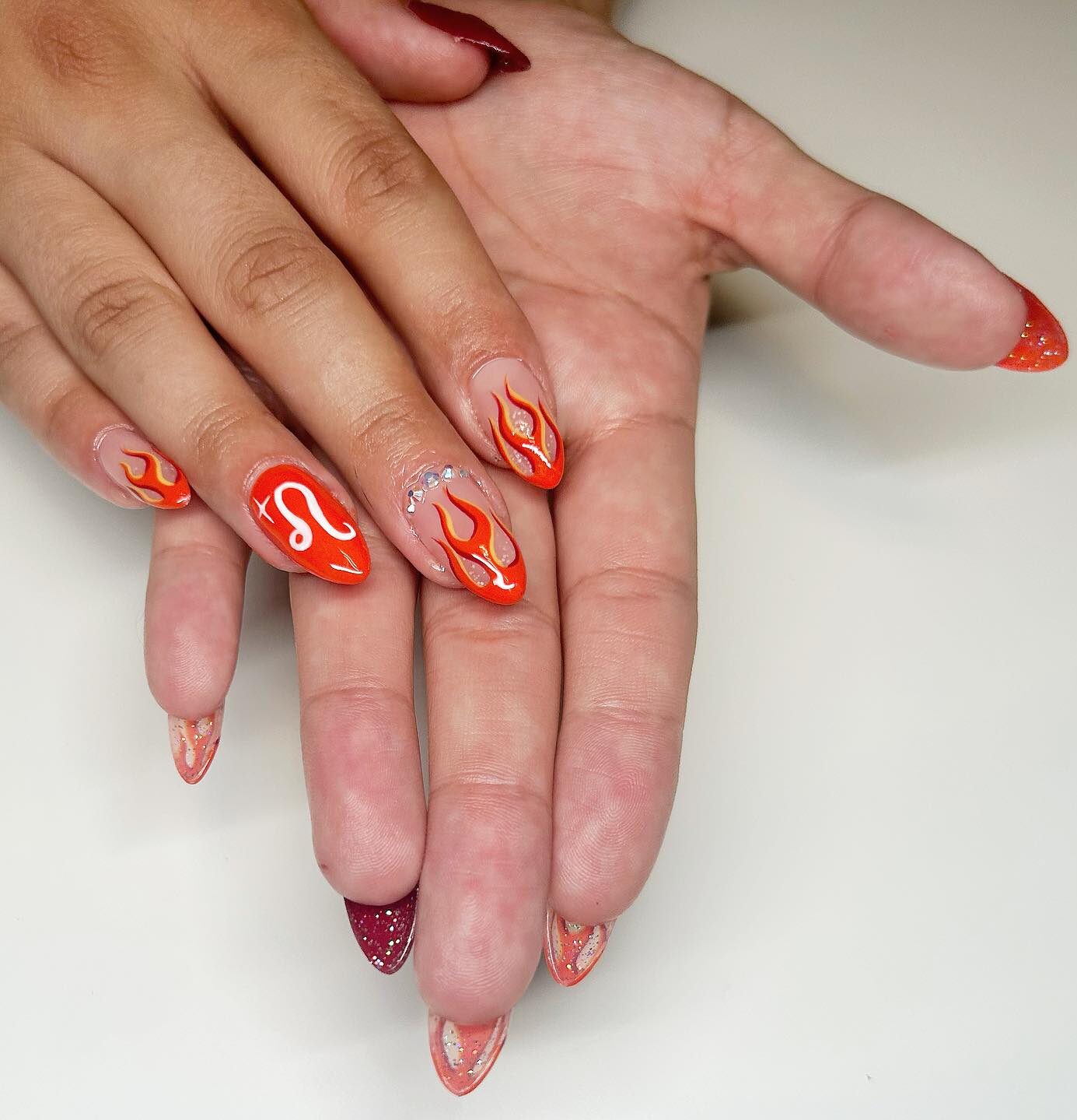 Diseño de uñas con llamas de color naranja vibrante y arte de uñas con el signo Leo en uñas redondas medianas