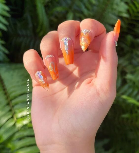 Elegante diseño de uñas naranja con gemas y pedrería en uñas largas de ataúd y stiletto