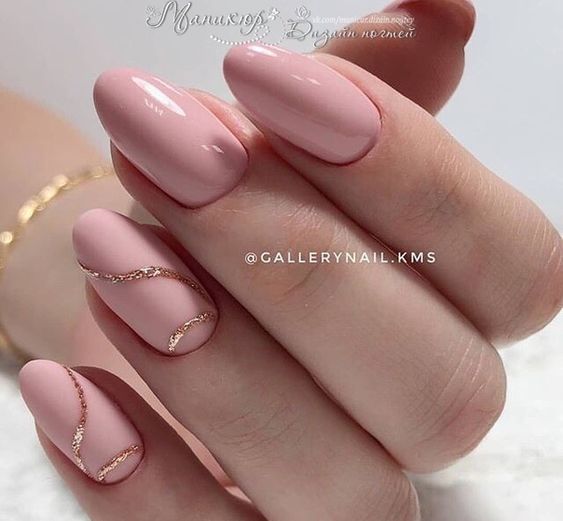 Esmalte de uñas rosa claro con remolinos dorados en uñas cortas y redondas