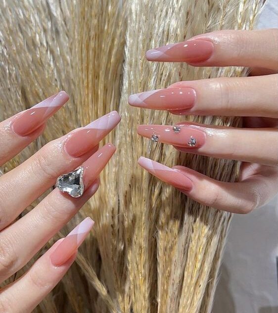 Color de uñas rosa pálido con elegantes puntas francesas de color rosa claro con piedras y gemas en uñas acrílicas largas en forma de ataúd.