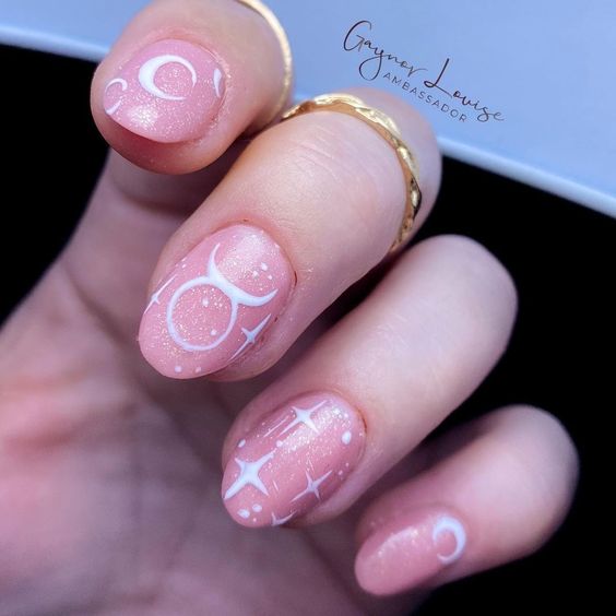 Esmalte de uñas con brillo rosa pálido con el signo de Tauro y elementos celestiales en uñas medianas y redondas