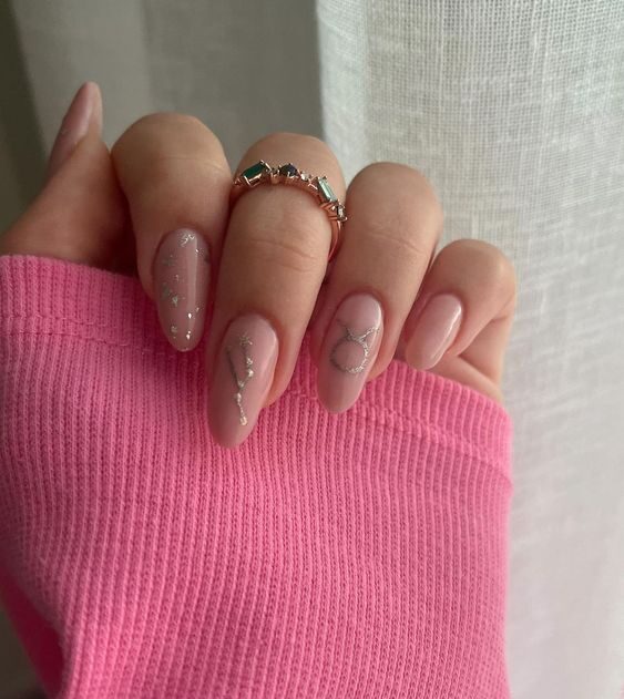 Esmalte de uñas de color rosa pálido con el signo de Tauro y la constelación de uñas en uñas largas y redondas