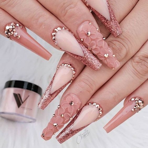 Uñas acrílicas largas y cuadradas con puntas francesas brillantes en oro rosa, pedrería y flores en 3D.