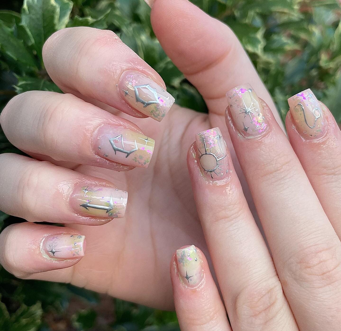 Color de uñas neutro con signo Leo plateado y decoración de uñas con elementos celestiales en uñas cuadradas cónicas medianas