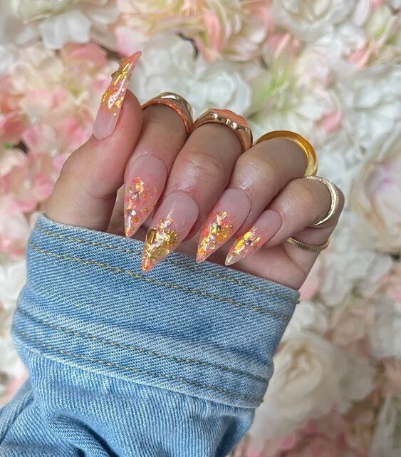 Elegante diseño de uñas con brillos naranjas en uñas acrílicas largas con forma de aguja