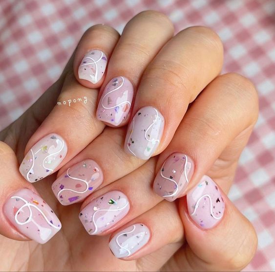Esmalte de uñas de color pastel con acabado brillante con remolinos blancos y brillos en uñas cortas de ataúd