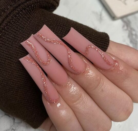 Esmalte de uñas rosa mate con remolinos de oro rosa brillante en uñas acrílicas cuadradas súper largas