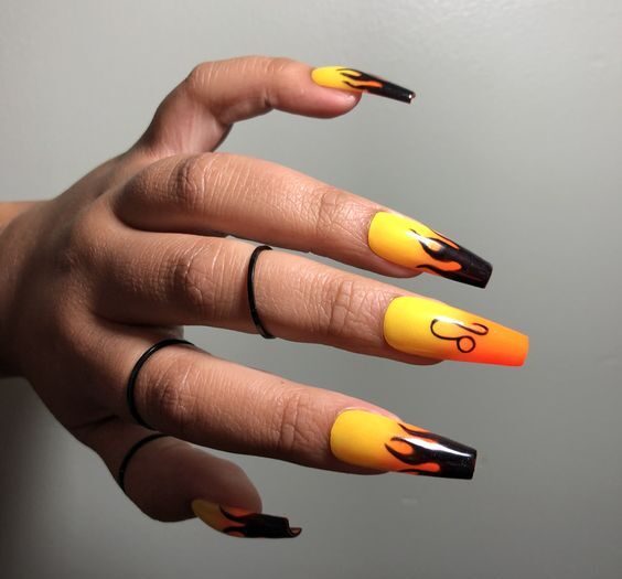 Efecto degradado de amarillo a naranja con llamas negras y diseños de uñas con el signo de Leo en uñas acrílicas largas con forma de ataúd
