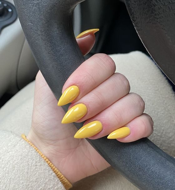Esmalte de uñas amarillo simple y liso en uñas largas de aguja