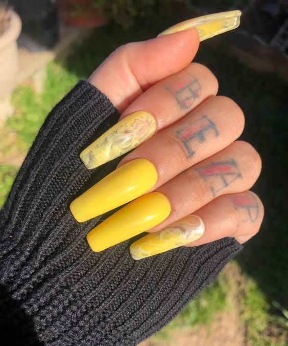 Esmalte de uñas amarillo y arte de uñas de mármol amarillo en uñas acrílicas largas con forma de ataúd