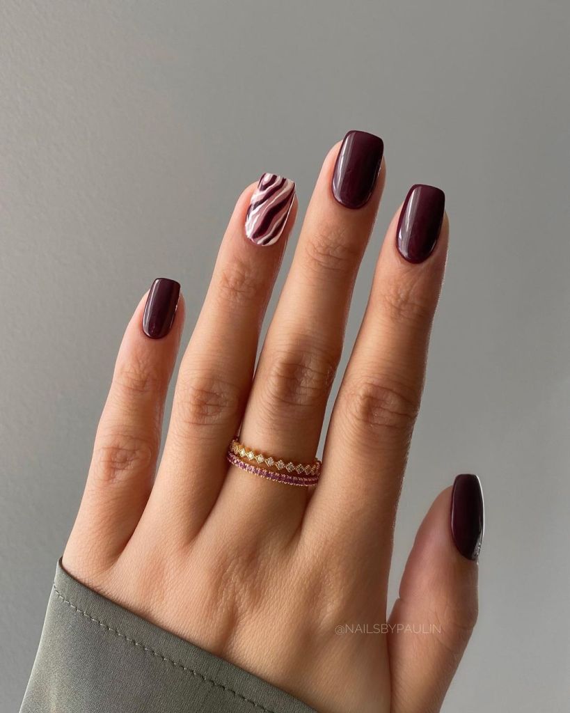 Uñas color burdeos con diseño de dedo anular con estampado de cebra