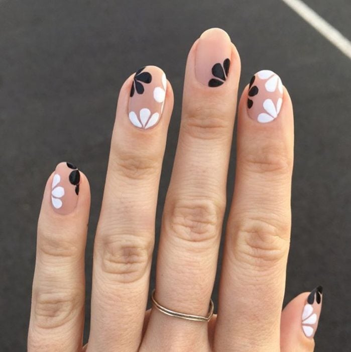 Mano de mujer con anillo dorado y uñas color carne adornadas con flores minimalistas y sencillas de color blanco y negro para la primavera