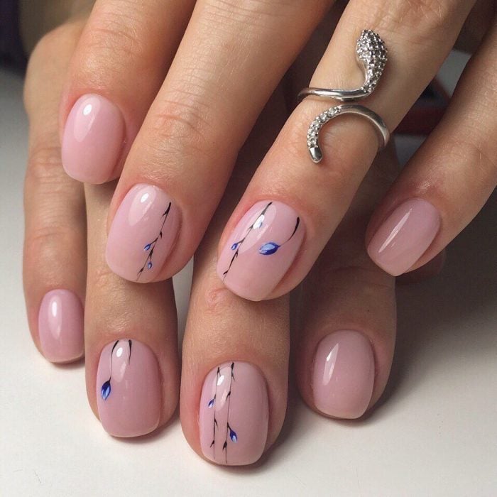 Manos de mujer con anillo plateado de serpiente con diamantes y uñas pintadas de rosa pálido con flores azules sencillas para la primavera