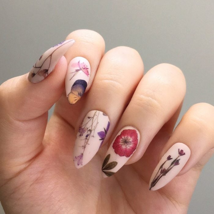 Mano de mujer con uñas largas con flores realistas pintadas de diferentes colores sobre una base rosa pálido mate para la primavera