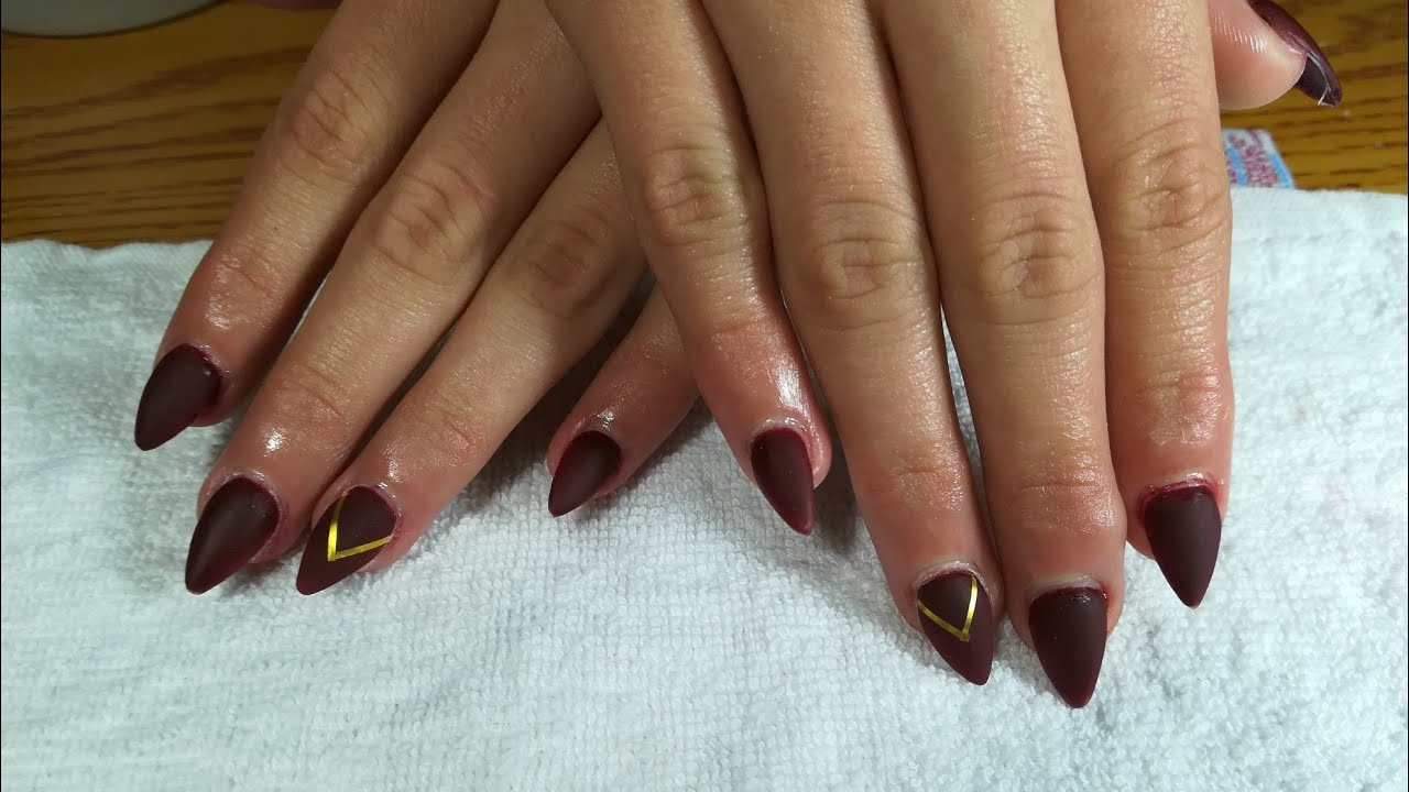 Uñas stiletto en color vino cintillo dorada 