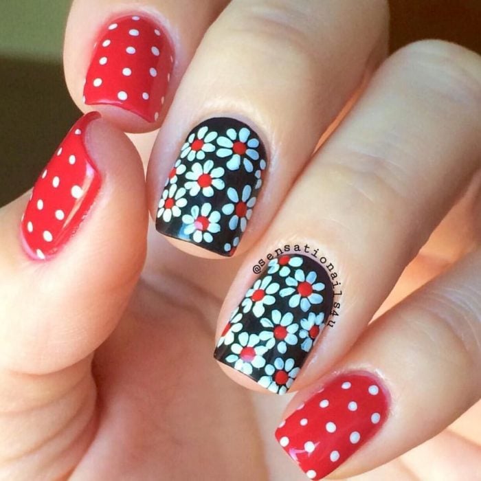 Mano de mujer con uñas pintadas de color negro y rojo, con estampado de flores y puntos blancos para la primavera